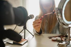 manos femeninas con aplicador de pincel de lápiz labial. mujer bloguera de belleza haciendo una revisión en video de productos cosméticos. foto