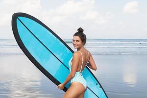 mujer joven con traje de baño a rayas con tabla de surf en la playa foto