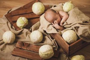 Little baby is lying in the box with a lot of cabbages around photo