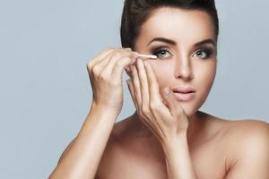 Beautiful young woman using cotton swab for make-up correction photo