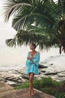 Young lovely woman wearing beautiful turquoise dress under the palm tree photo