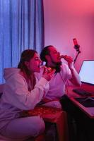 pareja relajándose en casa en una habitación con luz de neón y comiendo pizza, viendo películas en línea o jugando videojuegos foto