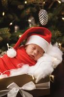 Cute newborn baby wearing Santa Claus hat is sleeping in the Christmas gift box photo