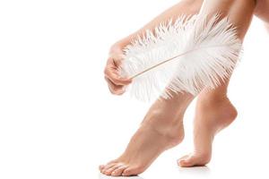 Female feet with smooth skin and soft ostrich feather on white background photo