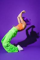 Carefree woman dancer wearing colorful sportswear performing against purple background photo