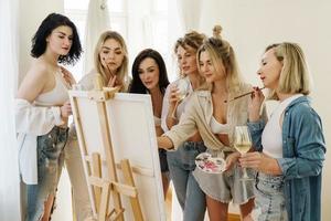 Group of women paint on canvas and drinking white wine during party at home photo