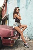 mujer sexy posando junto a un viejo coche oxidado en la calle foto