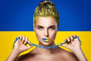 Strong woman with yellow blue lipstick and Ukrainian flag on background photo