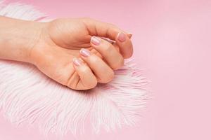 Female hand with smooth skin and soft ostrich feather on pink background photo