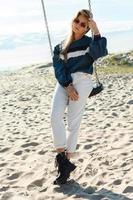 Young woman sitting on the swing at the sandy beach. photo