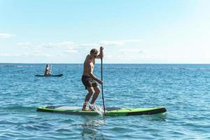 Young male surfer riding standup paddleboard in ocean. photo