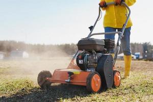 Woman villager is using aerator machine to scarification and aeration of lawn or meadow photo