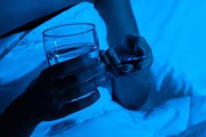 manos femeninas con un vaso de agua y pastillas para dormir foto