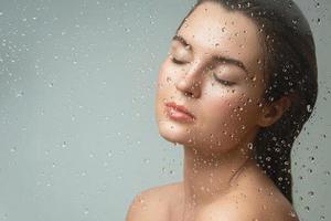 Woman behind the wet glass. Focus on the droplets. photo