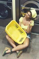 mujer sexy con una cesta amarilla sentada en el suelo en la lavandería foto