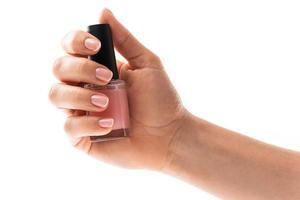 Female hands with beautiful french manicure holding bottle of pink nail polish against white background photo