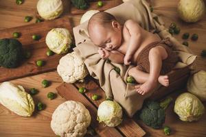 Little baby is lying in the box with a lot of different cabbages photo