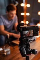 Blogger sitting on sofa in front of a camera is working on his laptop photo
