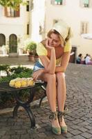 Woman is sitting on the bench in the shade of a tree with a string bag of lemons. photo