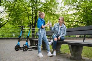 madre e hija con scooters eléctricos están bebiendo limonada en el parque de la ciudad foto