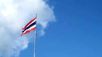 Photograph the Thai flag with three colors red white and blue in a slow motion on a tall pole against the sky. a little cloudy The wind blows the flag fluttering in the wind. video