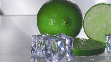 The green lemon is blank with a cut piece showing the inside of the citrus zest. The clear glass reflects the shadows of the lemon and the wet water, giving it freshness and ice adding cooling. video