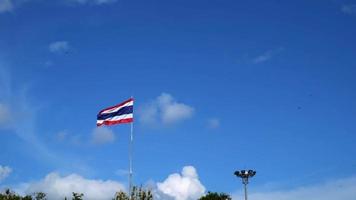 Photograph the Thai flag with three colors red white and blue in a slow motion on a tall pole against the sky. a little cloudy The wind blows the flag fluttering in the wind.