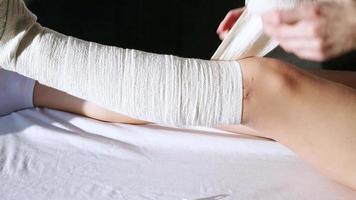 femme après une chirurgie du genou mettant un bandage sur le canapé. femme portant une orthèse de genou ou une attelle de soutien du genou après une intervention chirurgicale sur la vue de face de la jambe video
