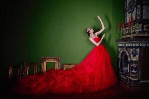 hermosa mujer con vestido rojo largo y corona real cerca de la chimenea en interiores de lujo en estudio fotográfico foto