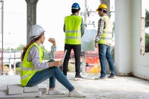 Asian engineer or Young woman Architect put on a helmet for safety and look at Blueprint in laptop for Inspect Building factory Construction Site and use talk with a contractor photo