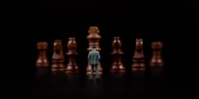 Figures businessman standing in front of wooden chess on black isolated background. Concept of business analysis and strategy. Stepping into the startup, new business player photo