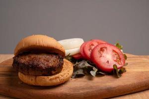 fresh tasty homemade hamburger with fresh vegetables, lettuce, tomato, cheese beside sliced tomatoes on a cutting board. Free space for text photo