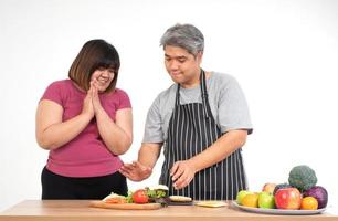 Happy overweight couple cooking a burger in the kitchen room. A vegetable on the table. Concept of happy family and binge eating photo