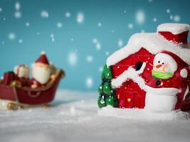 Happy Santa Claus with gifts box on the snow sled going to snow house. near snow house have Snowman and Christmas Tree. Santa Claus and snow house on the snow the background is powder blue. photo