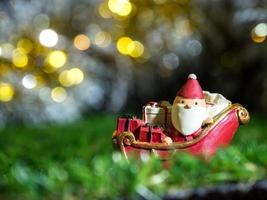 feliz santa claus con caja de regalos en el trineo de nieve el fondo es decoración navideña.santa claus y decoración navideña en hierba verde. feliz navidad y feliz año nuevo concepto foto