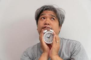 Asian middle-aged man is holding a white alarm clock and his face showed boredom and feeling bad, his problem is a sleep disorder. The concept of suffering insomnia photo