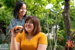 The overweight woman is in a wheelchair. Being eating a burger in which but her friend is not happy because of concern for the health of a friend. Health and care of best friend concept. photo