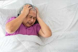 Senior woman with gray hair in bed feel depressed or suffering from strong headache migraine and high blood pressure, insomniac trying to sleep disturbed toss and turn in bedroom