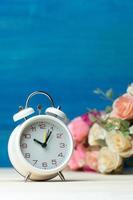 White alarm clock and flowers pink and red rose on wooden table and blue background with copy space for add text and content. photo