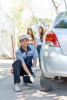 Expertise mechanic man  in uniform using force trying to unscrew the wheel bolts nuts and help a woman for changing car wheel on the highway, car service, repair, maintenance concept. photo