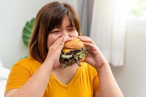 Hungry overweight young asian woman holding hamburger, Her hungry all time and overeat, gluttony and binge eating. Her lifestyle is eating fast food all time. Unhealthy Concept photo