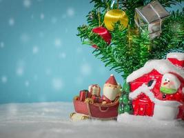 feliz santa claus con caja de regalos en el trineo de nieve yendo a casa. cerca de la casa hay un muñeco de nieve y un árbol de navidad. santa claus y casa en la nieve. concepto de navidad y feliz año nuevo. foto