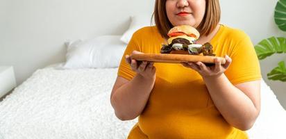 Hungry overweight young asian woman holding hamburger, Her hungry all time and overeat, gluttony and binge eating. Her lifestyle is eating fast food all time. Unhealthy Concept photo