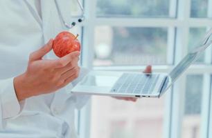 los médicos o nutricionistas sostienen manzanas y computadoras portátiles en la clínica para explicar los beneficios de las frutas y verduras. la buena salud comienza contigo. concepto de comida útil. foto
