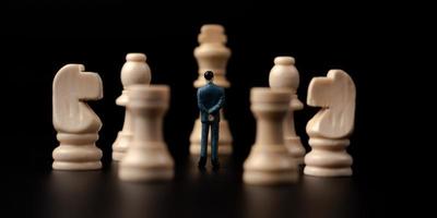 Figures businessman standing in front of wooden chess on black isolated background. Concept of business analysis and strategy. Stepping into the startup, new business player photo