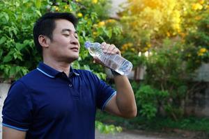 un apuesto hombre asiático sostiene una botella de agua potable para beber al aire libre. concepto, agua potable para la salud, estilo de vida saludable. saciar la sed, reducir la fatiga, refrescar el cuerpo. foto