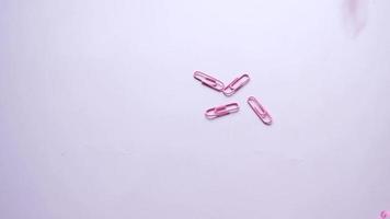 Pink paper clips fall on table in slow motion video