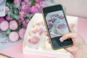 foto por teléfono de pastelitos recién hechos y hermosas flores en una mesa.