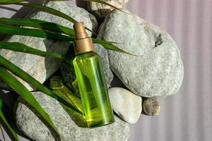 A bottle of green color with a spray bottle lies on the stones, next to the green leaves photo