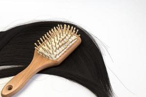 Hair care wooden comb on a long strand of black hair on a white background. Tools from biological materials and natural hair.